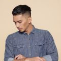 Asian man with slicked back hair wearing a denim polo