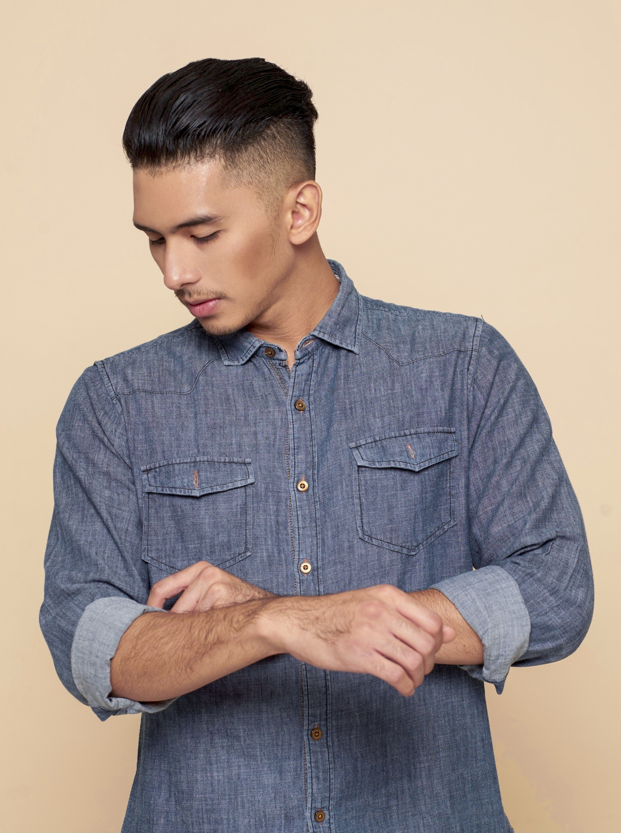 Asian man with slicked back hair wearing a denim polo