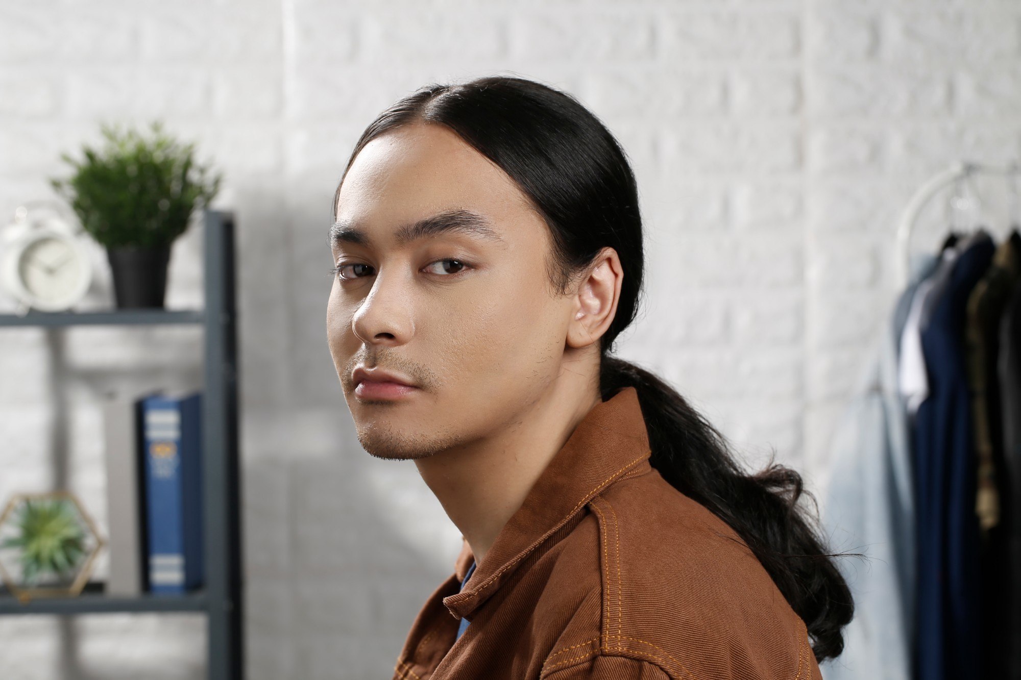 how to style men's long hair: guy wearing a brown jacket is looking at the camera with his low man ponytail
