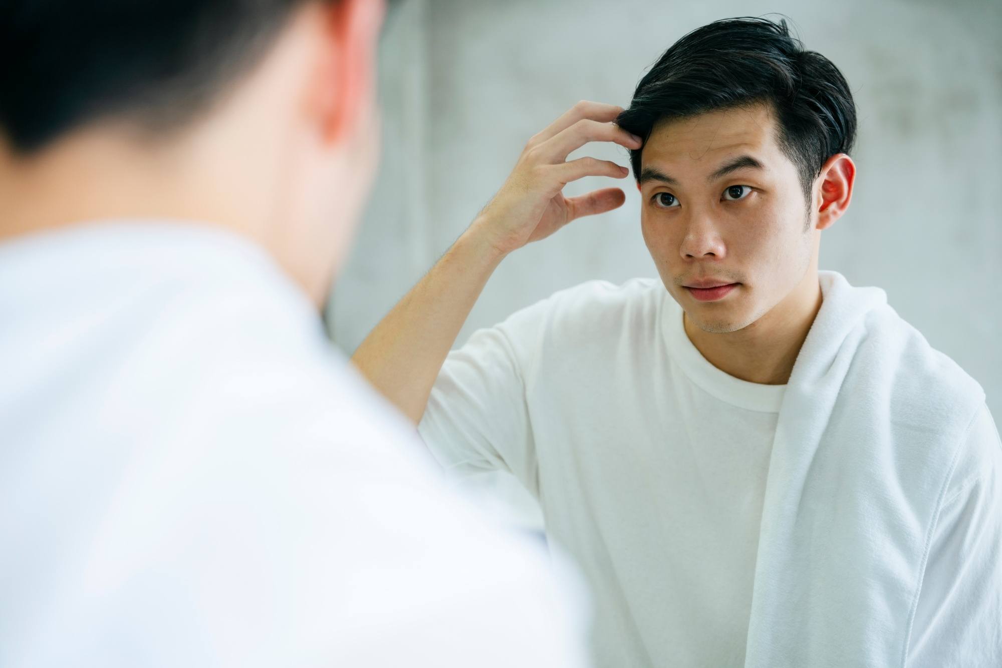 Asian man looking in the mirror and touching his hair