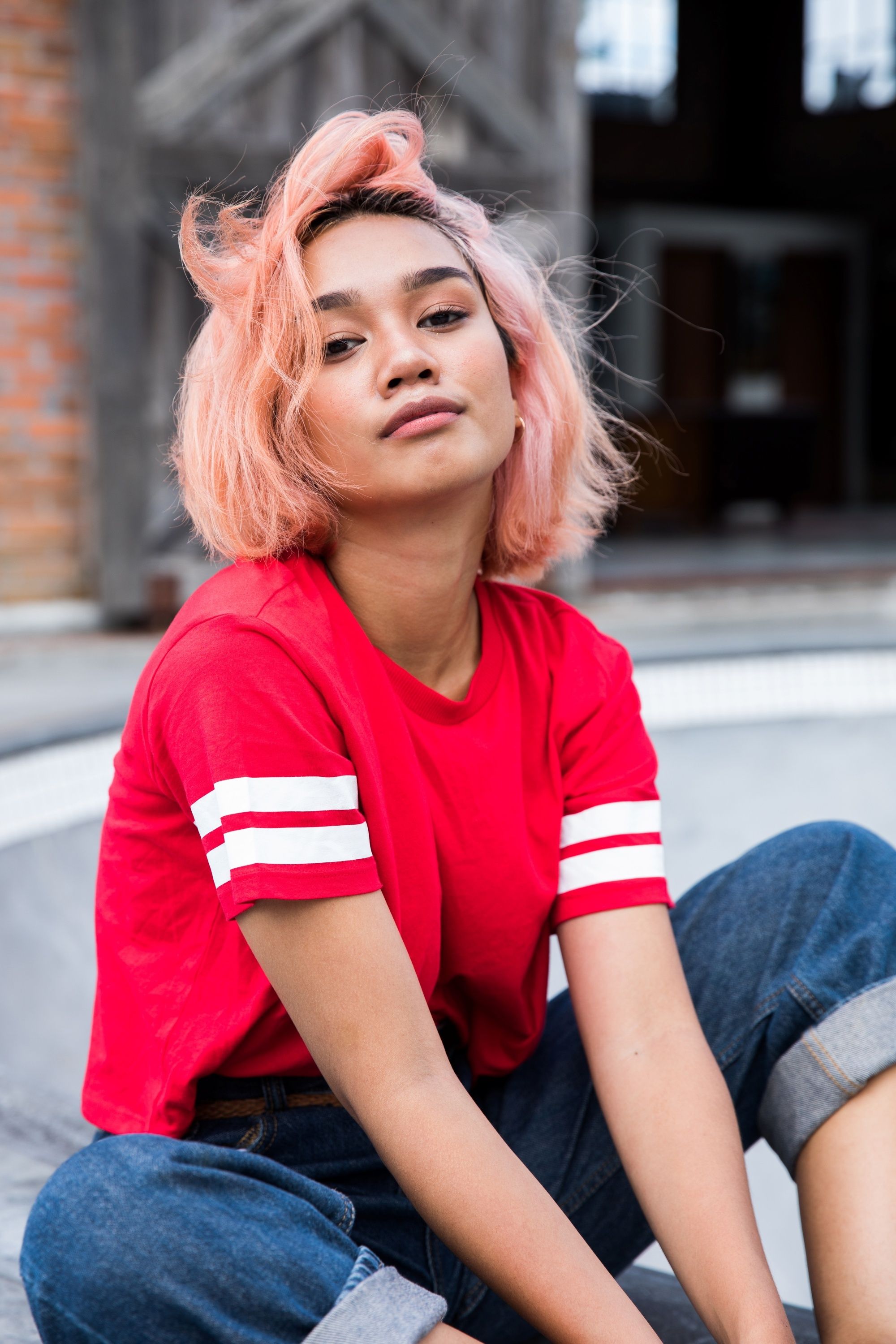 Asian woman with short light coral pink hair wearing a red shirt