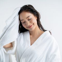 Asian woman wearing a white robe towel-drying her newly washed hair