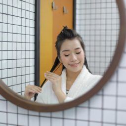 Asian woman looking in the mirror applying natural oils for hair growth