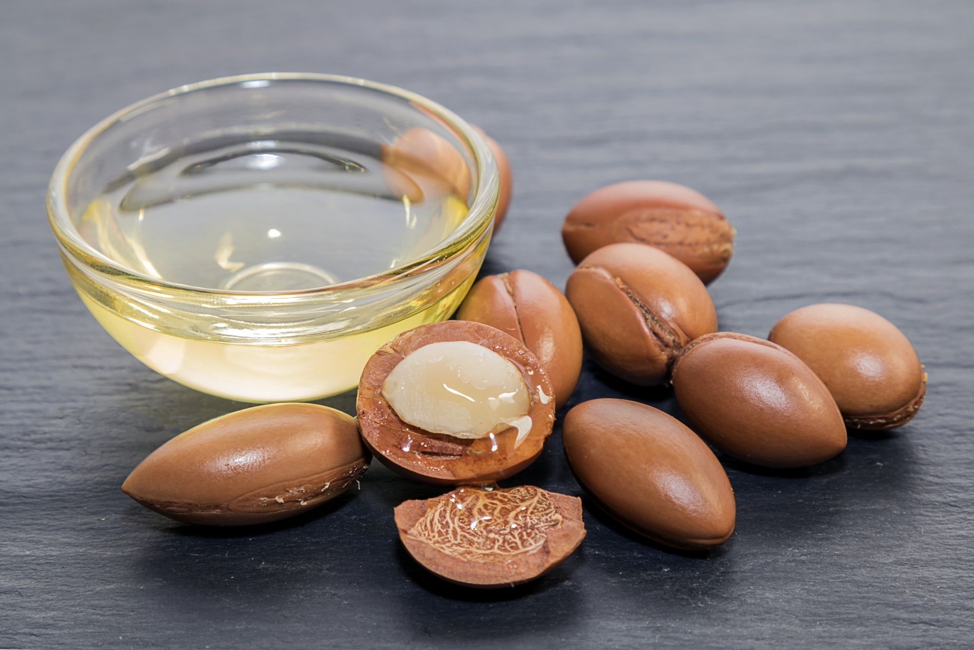 A bowl of argan oil and argan kernels on a gray table