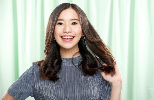 Hair fall treatment: Asian woman smiling and touching her long hair