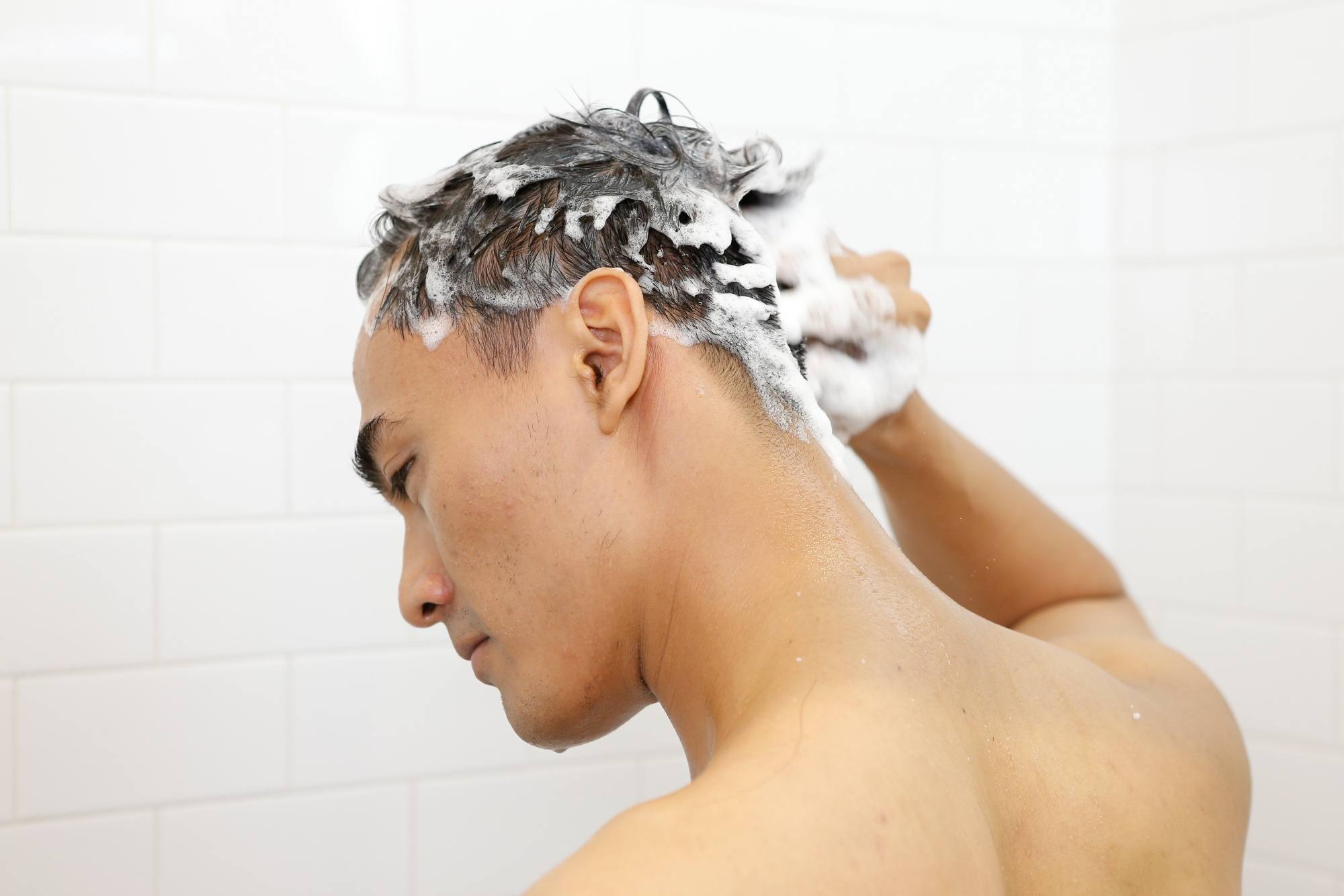 Asian man washing his hair with an anti-dandruff shampoo