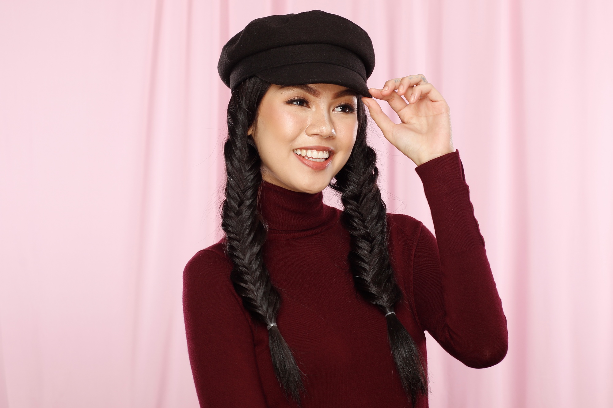 Asian woman with twin fishtail braids wearing a newsboy hat