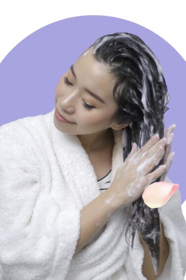 Natural beauty: Asian woman shampooing her hair with petal elements around her