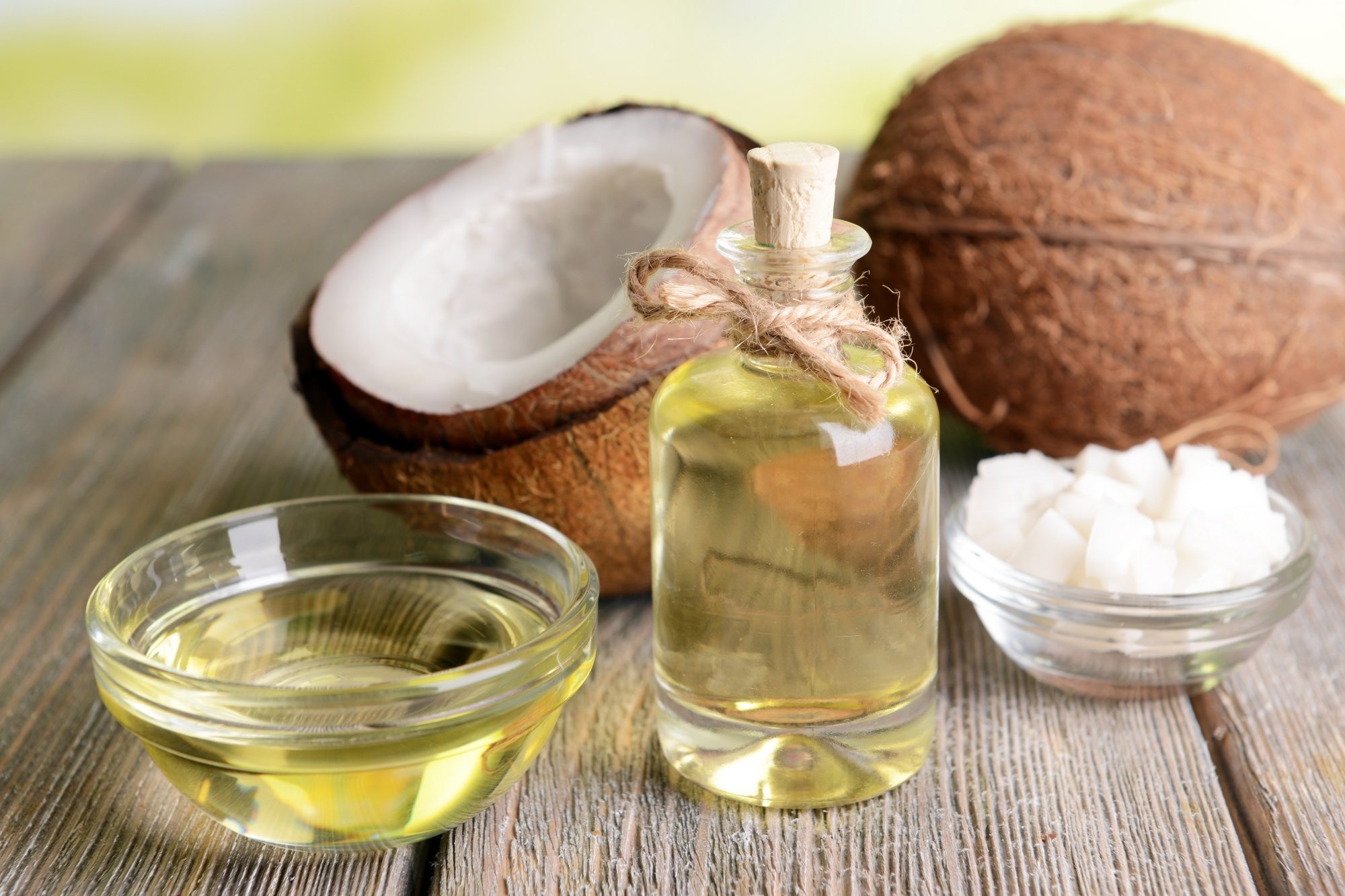 A bottle and bowl of coconut oil and sliced coconuts on a table