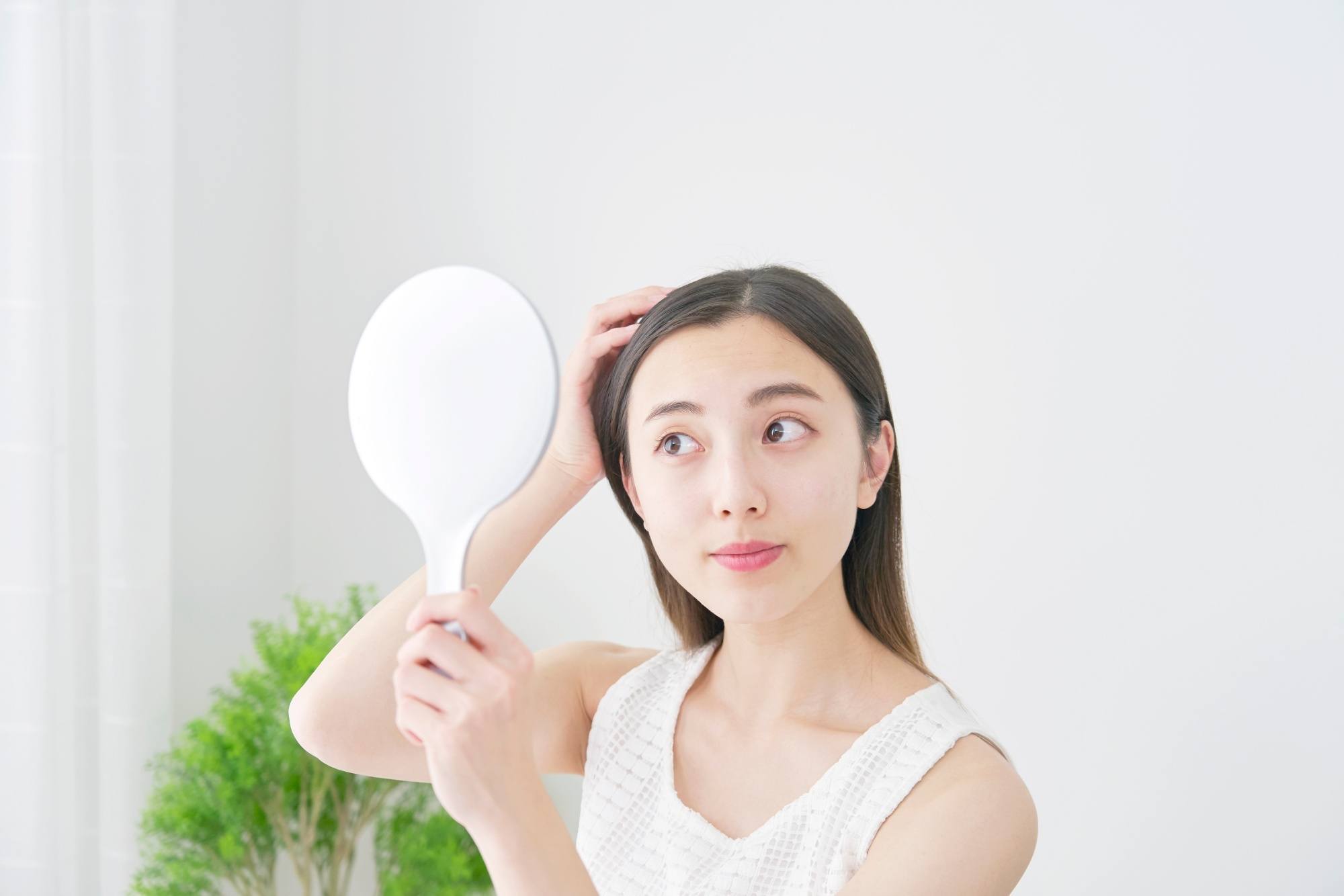 Asian woman looking in a mirror checking her scalp for dandruff