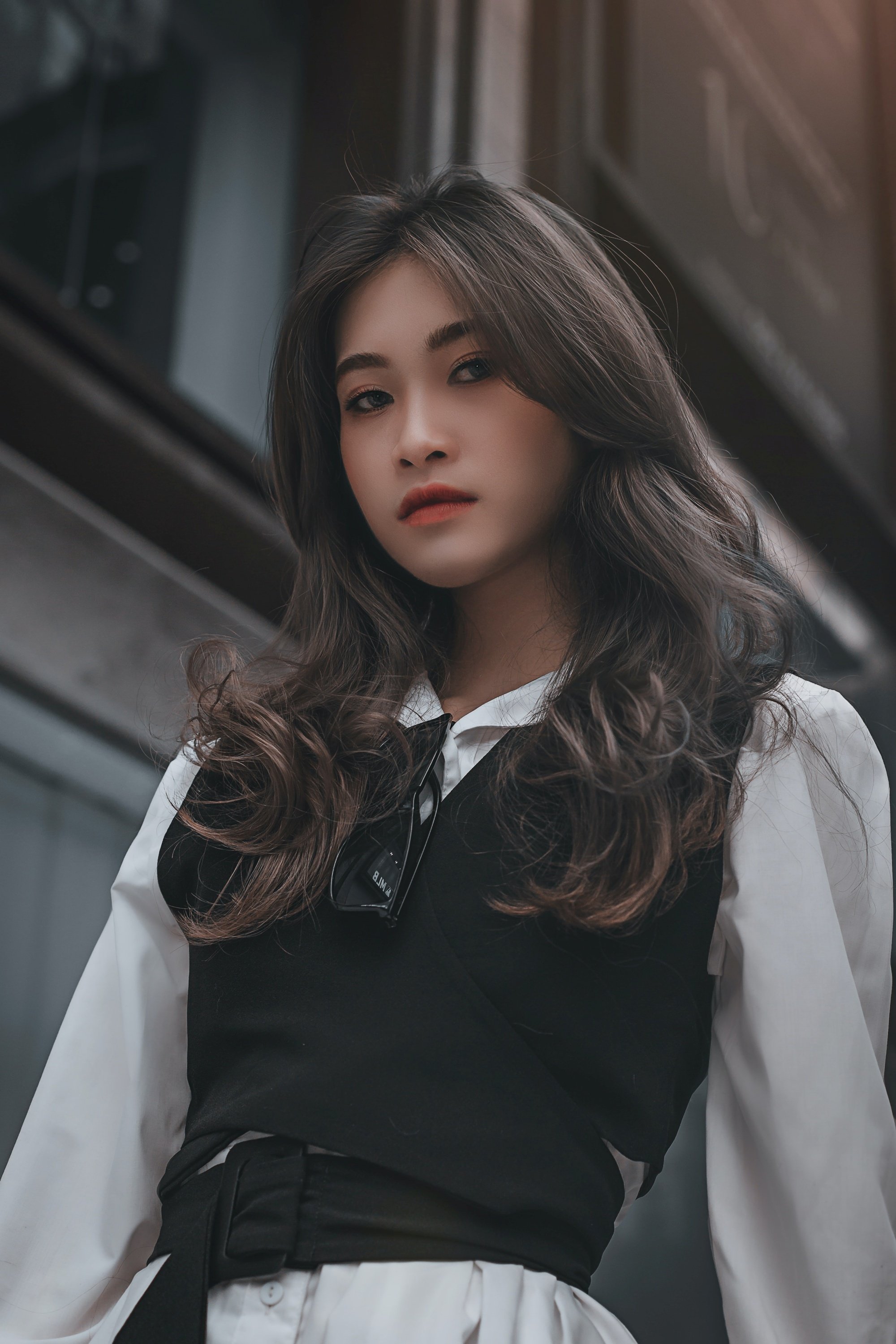 Asian woman with long layered hair wearing a black vest and a white long-sleeved blouse