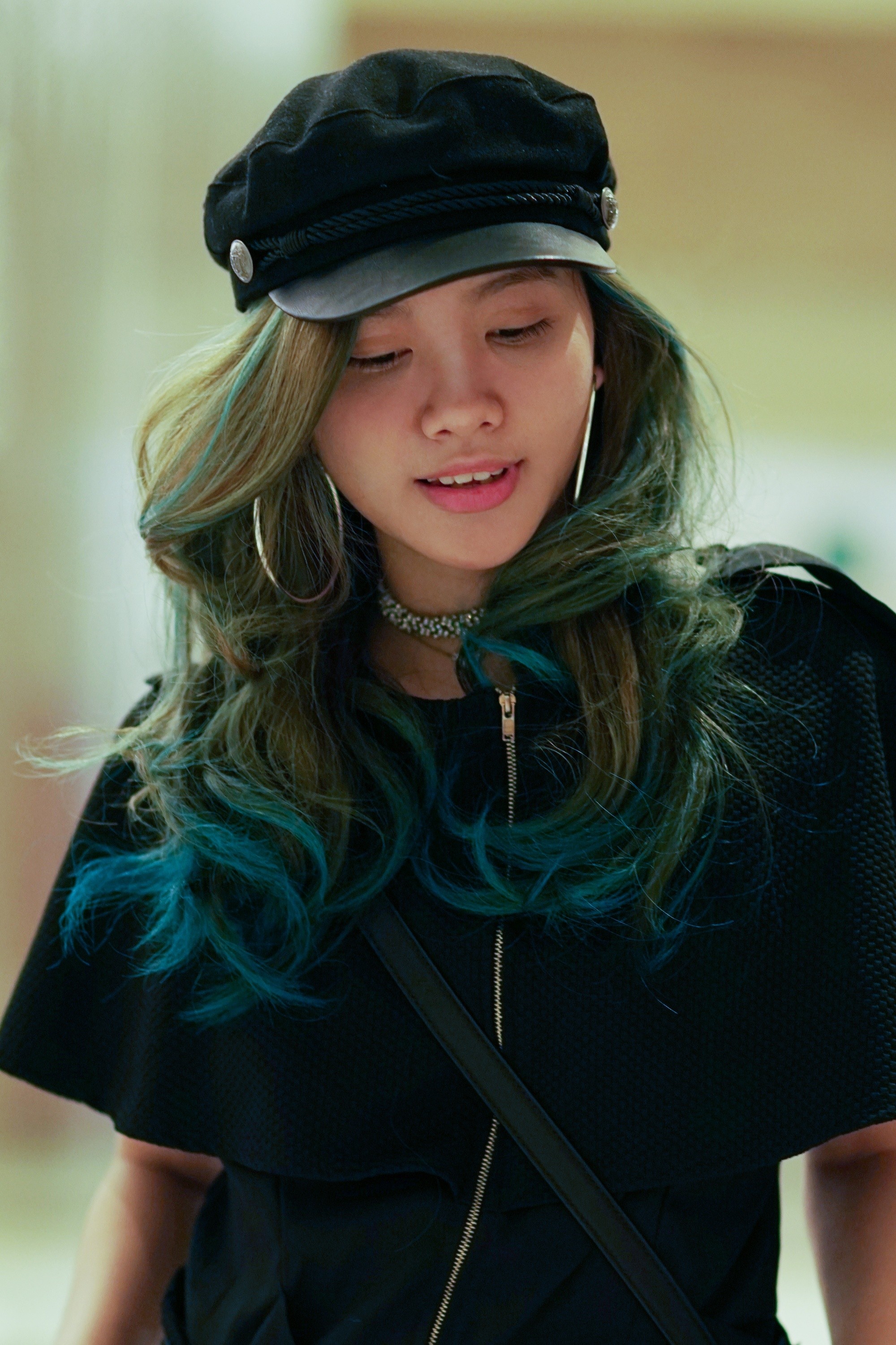 Asian woman with blue and green hair wearing a newsboy cap