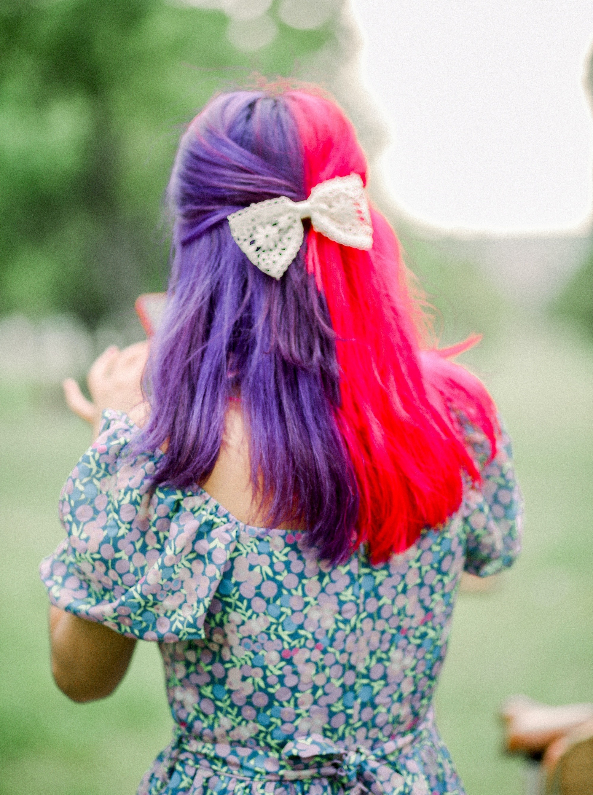 Back of a woman with pink and purple hair with a white ribbon