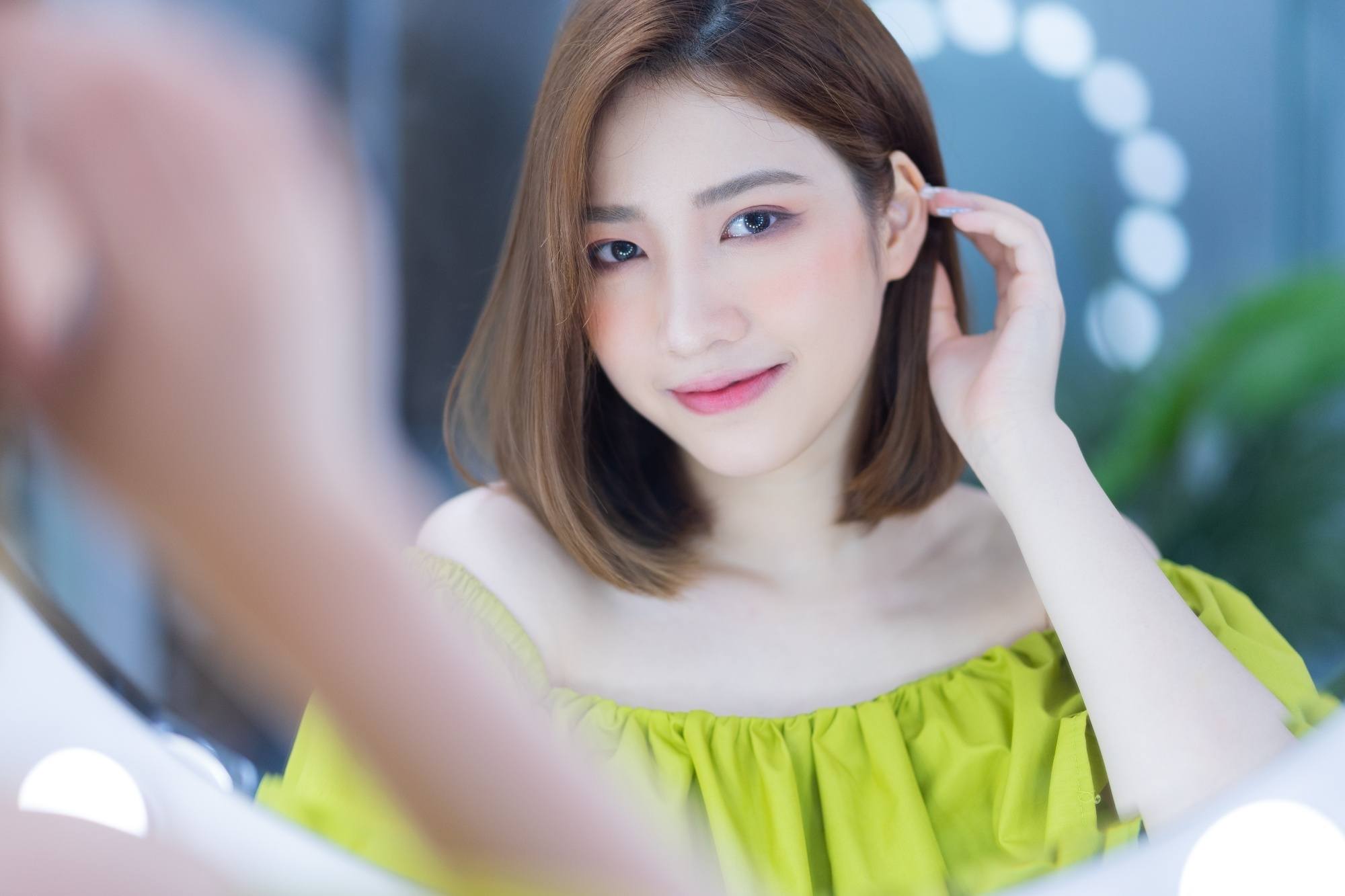 Asian woman looking in the mirror testing hair theory and tucking her short hair behind her ear