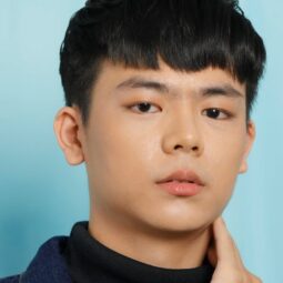 Asian man with dark hair wearing a dark turtleneck shirt posing for a photo about what causes dandruff