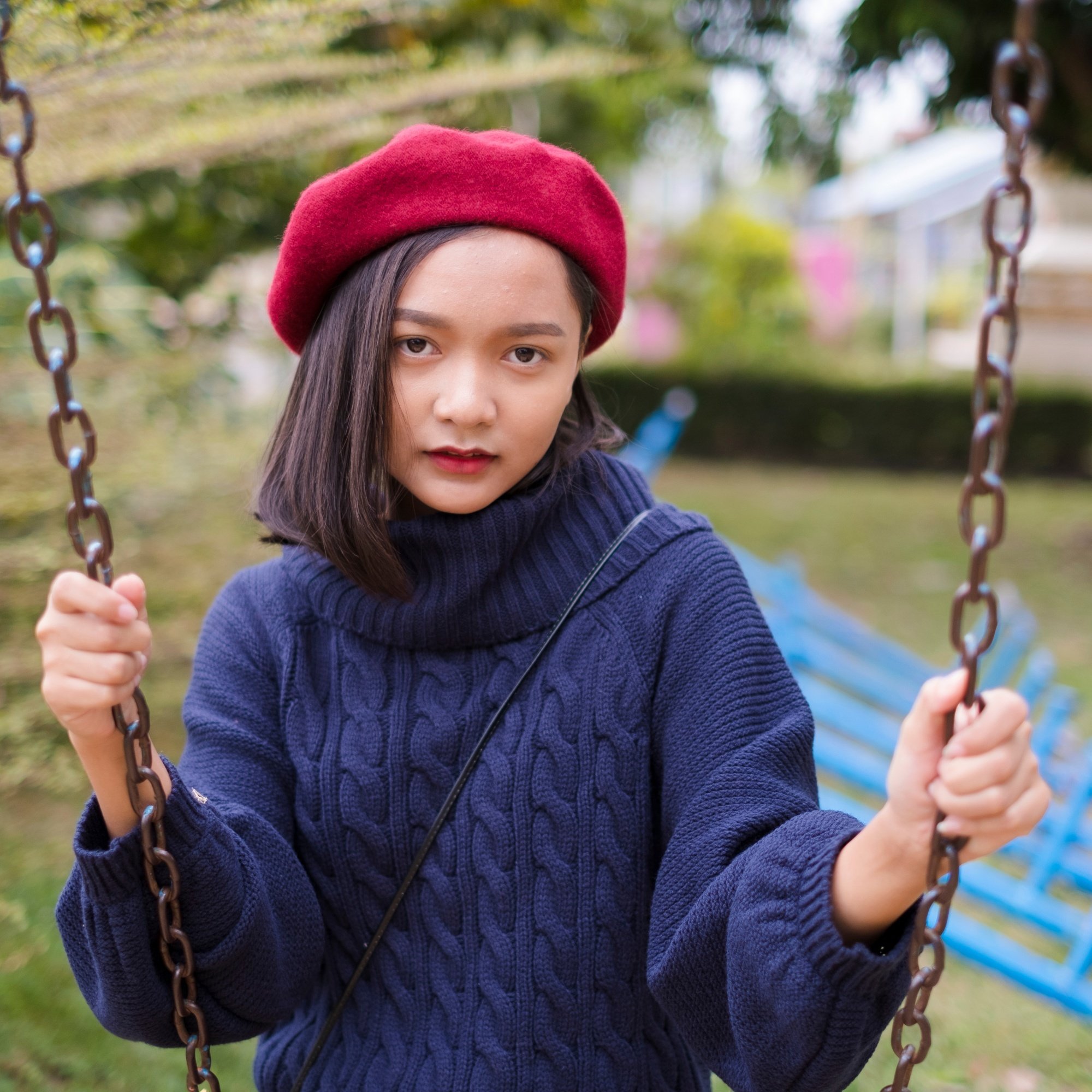 Asian woman with short hair wearing a red beret and sitting on a swing