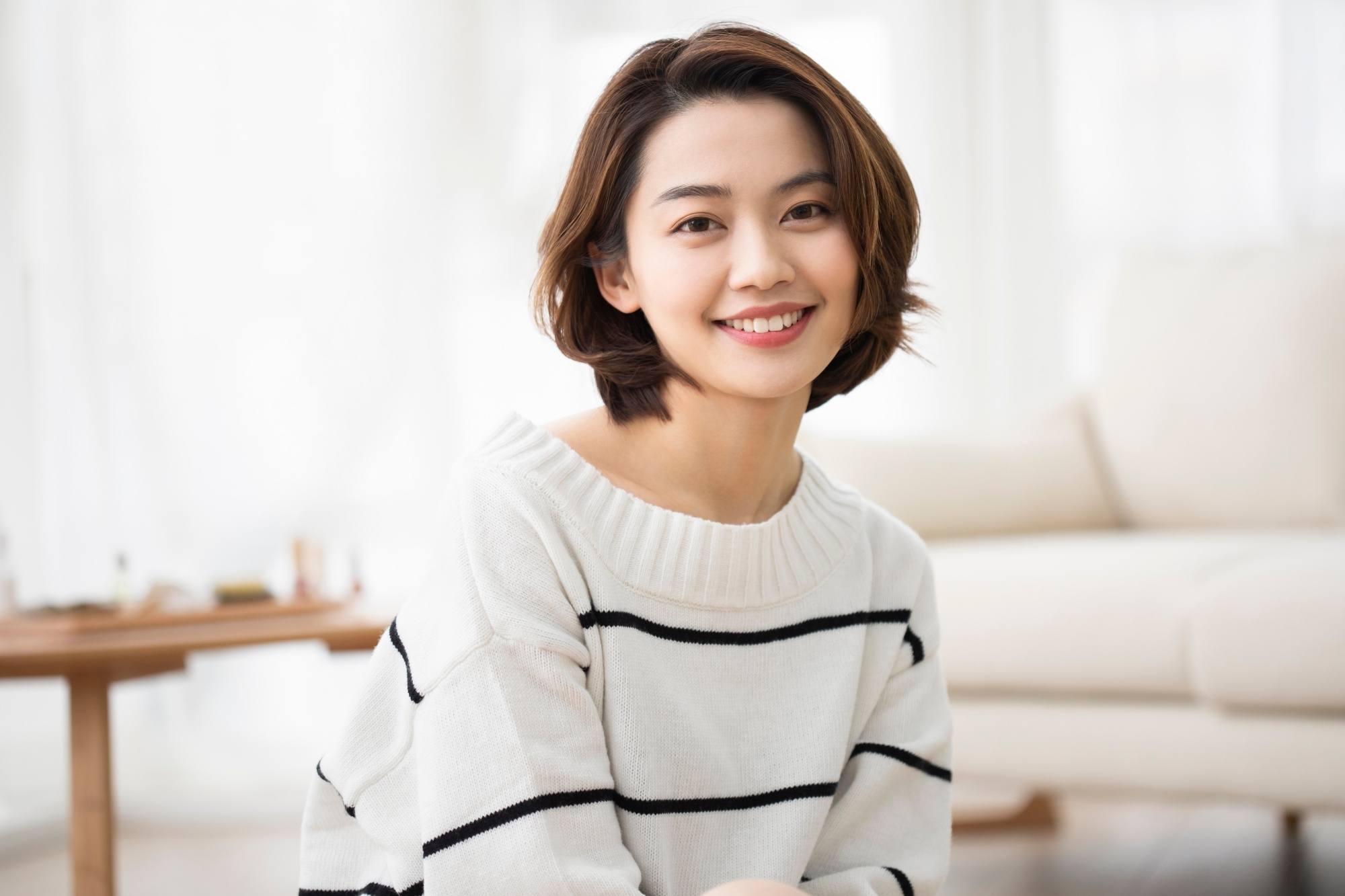Asian woman with short hair wearing a long-sleeved shirt in a living room