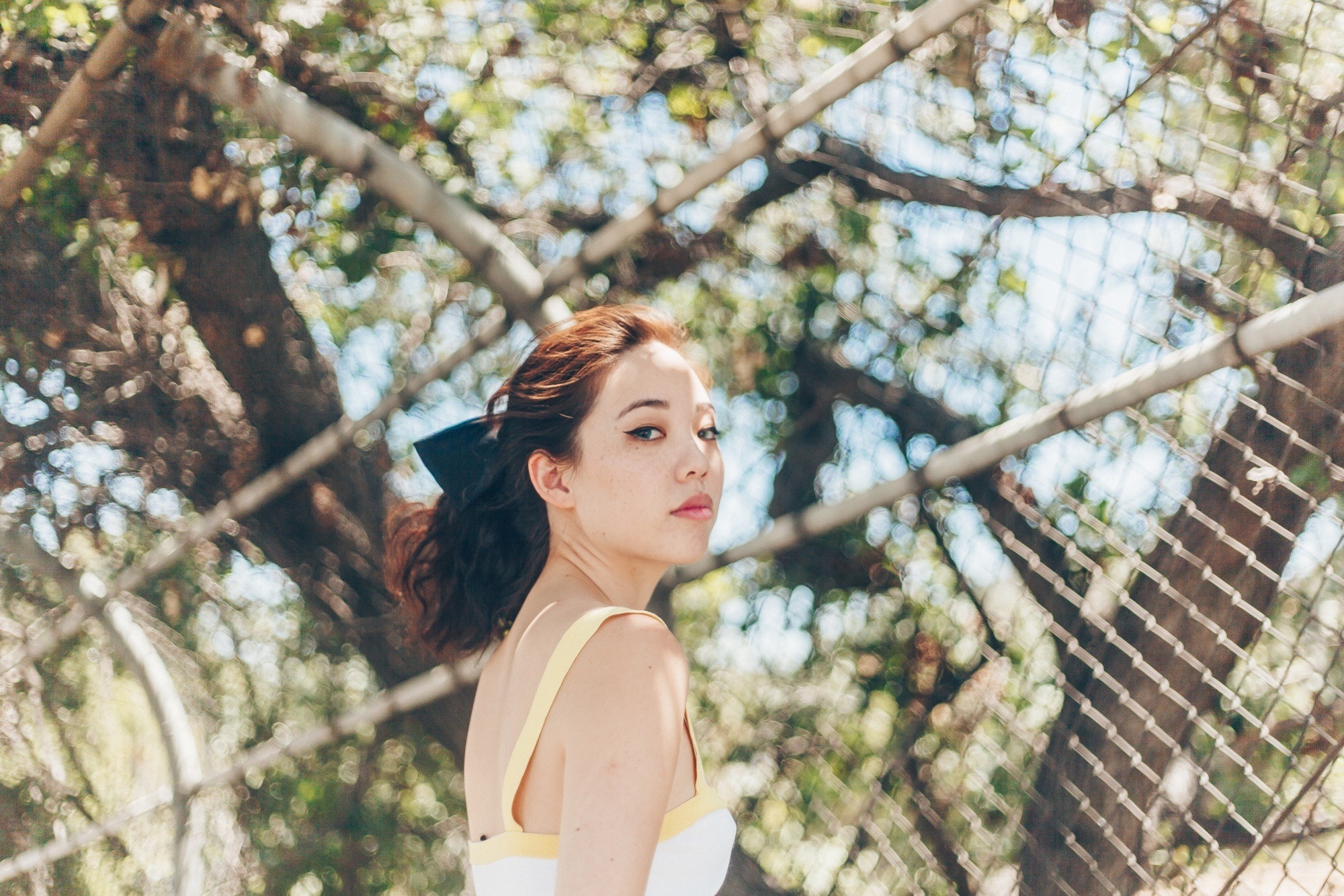 Asian woman with shoulder-length wavy hair in a ponytail wearing a light yellow sleeveless dress