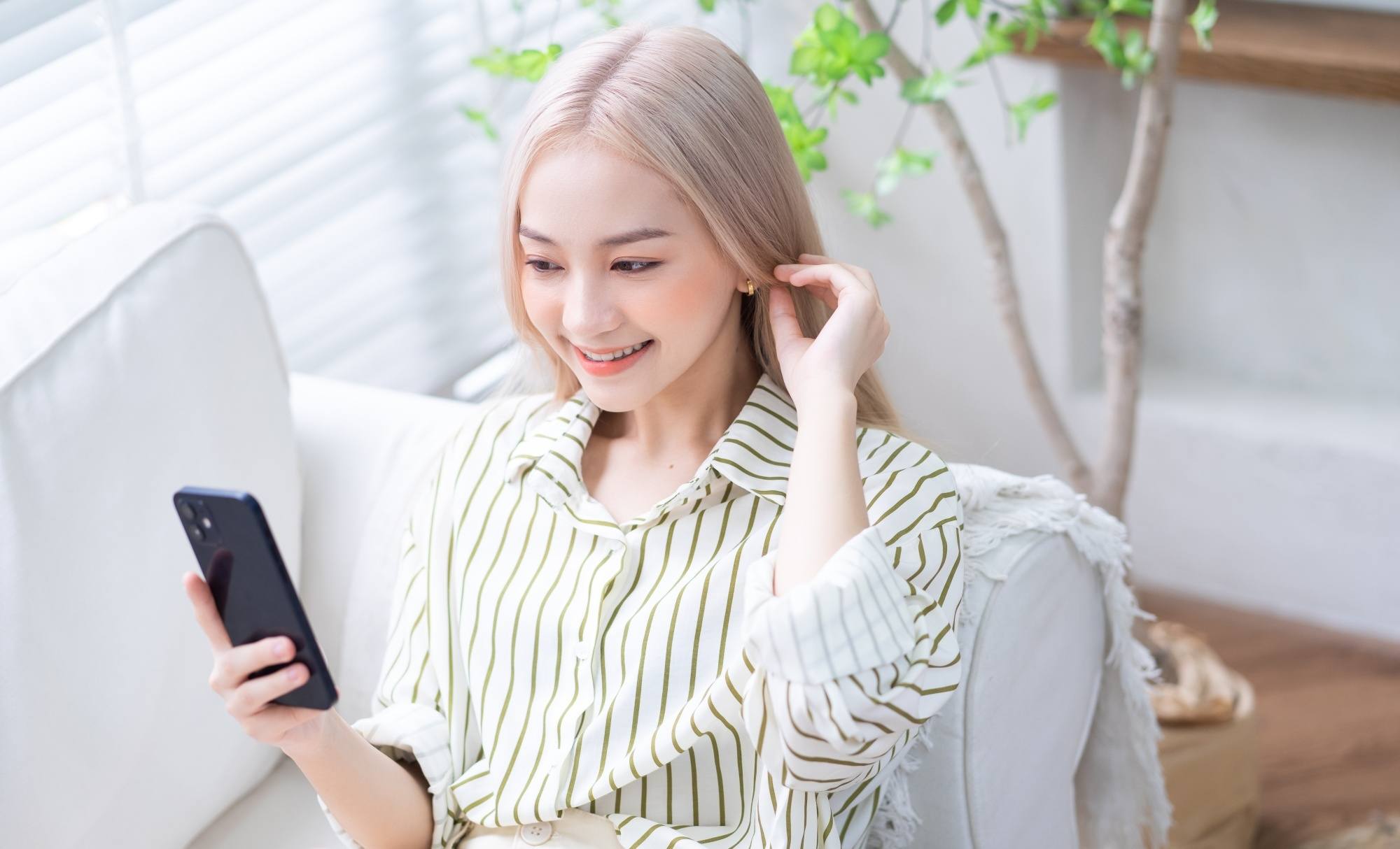 Asian woman with blonde hair using her mobile phone while sitting on a sofa