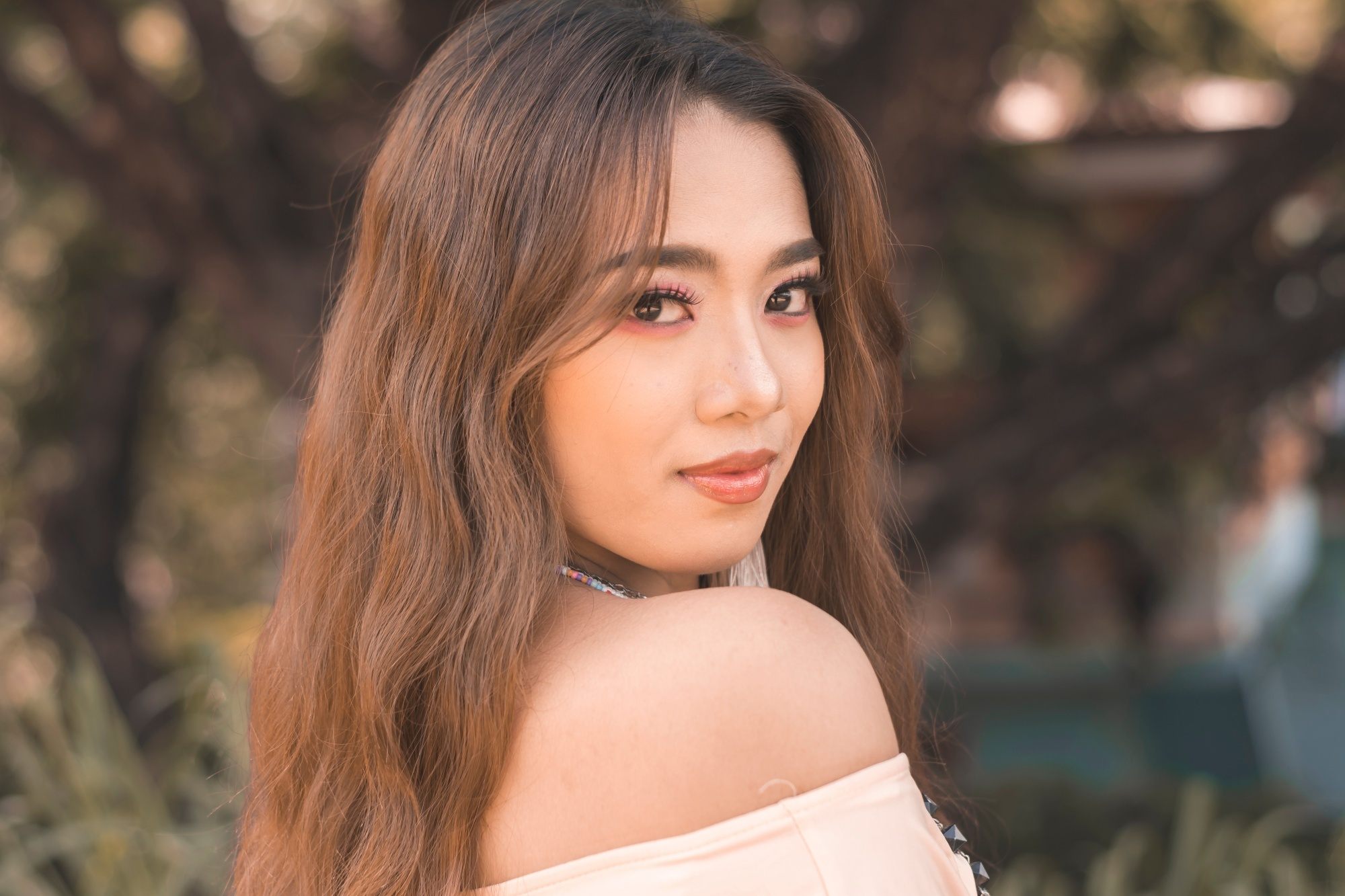 Asian woman with long wavy brown hair wearing an off-shoulder top