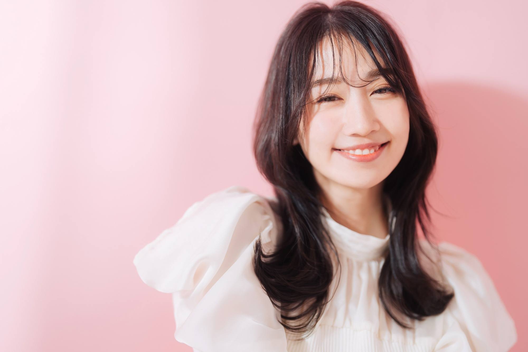 Asian woman with a long jellyfish haircut with see-through bangs wearing a white top.