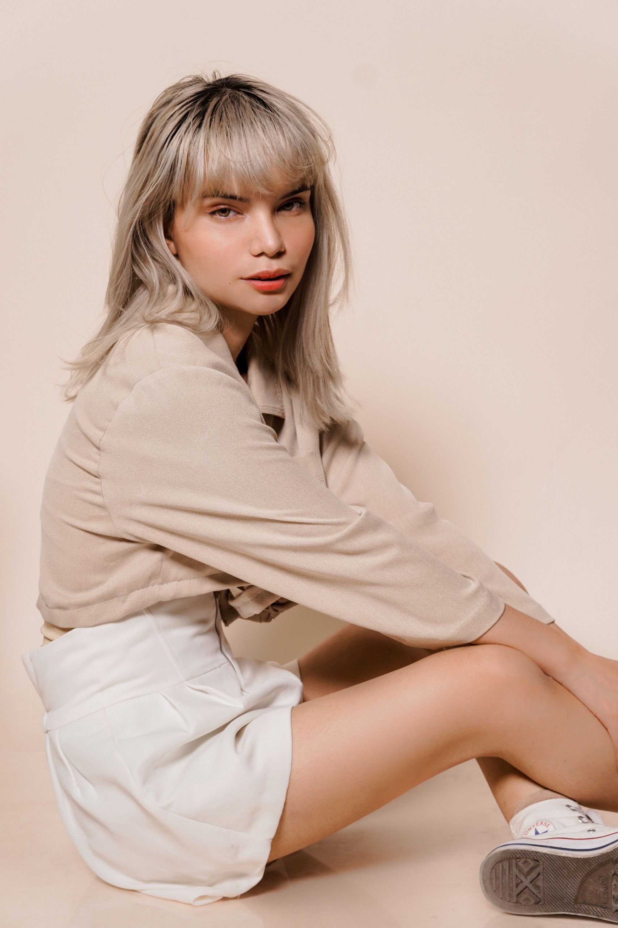Asian woman with dark blonde hair color and bangs wearing a beige long-sleeved blouse.