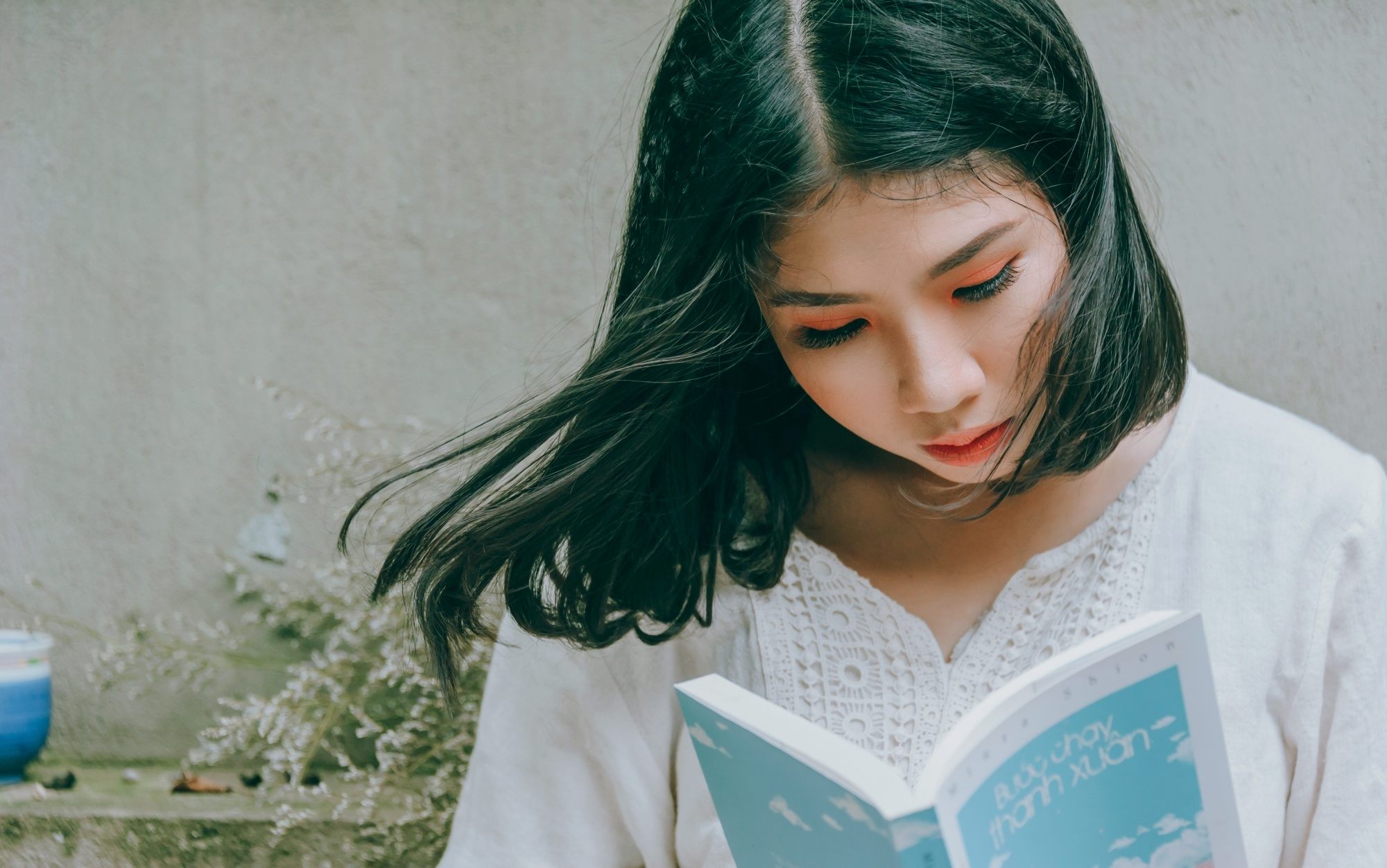 Asian woman with black hair with green highlights reading a book.