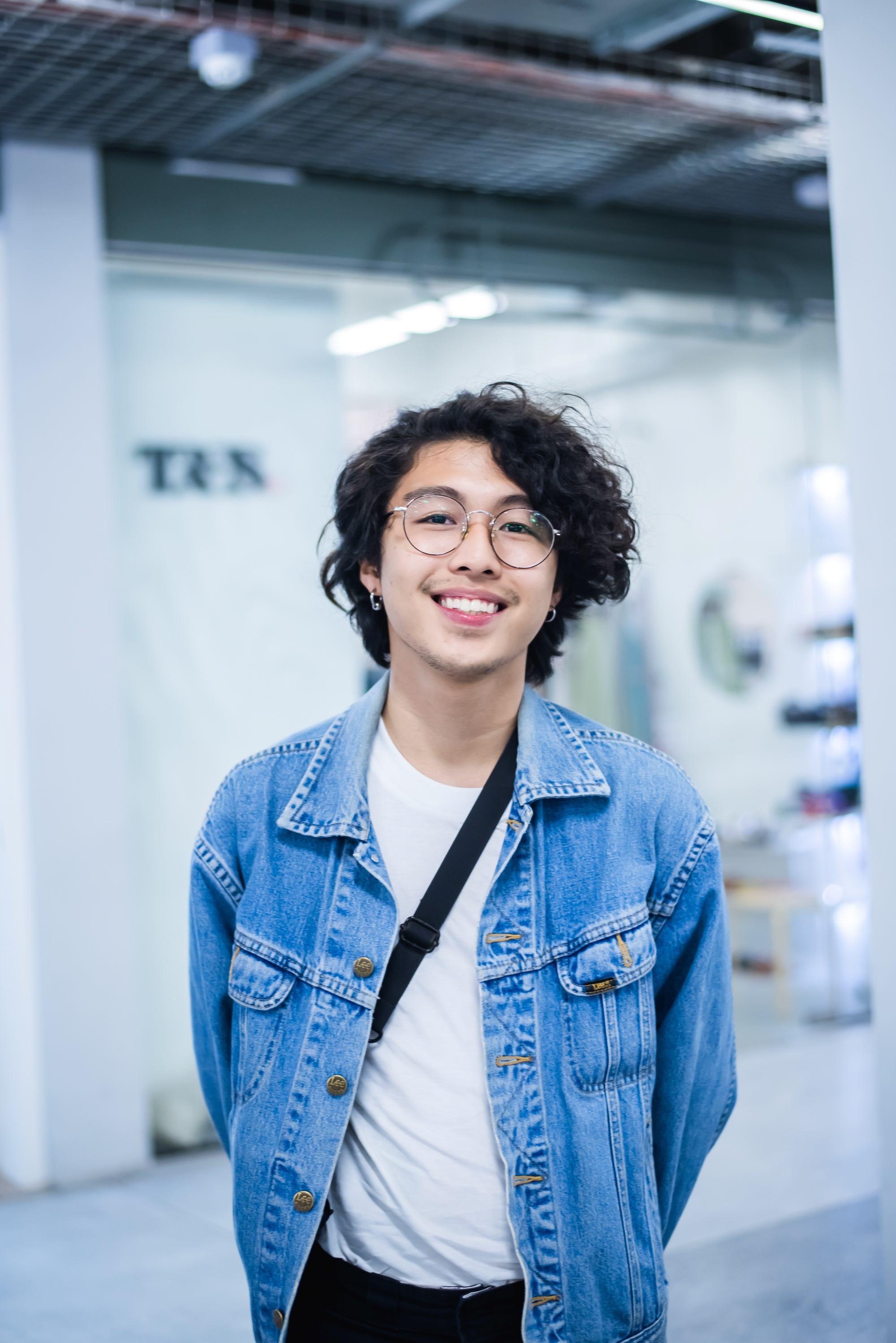 Asian man with a curly wolf cut wearing eyeglasses and a denim jacket.