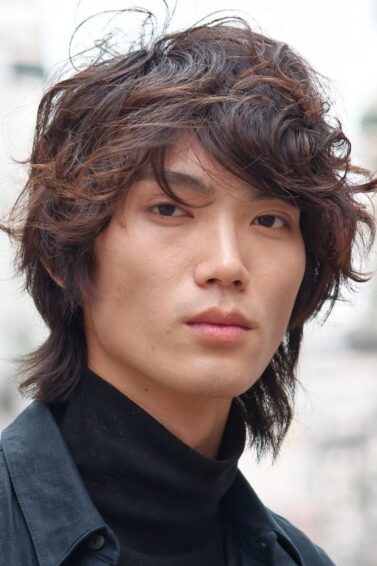 Asian man with a curly wolf cut hair wearing a black turtleneck shirt.