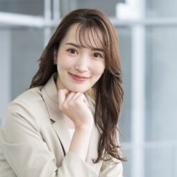 Asian woman with a long, wavy Japanese hairstyle wearing a beige suit.