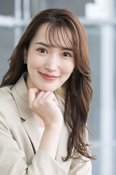 Asian woman with a long, wavy Japanese hairstyle wearing a beige suit.