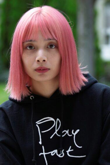 Asian woman with short pink hair wearing a black hoodie.