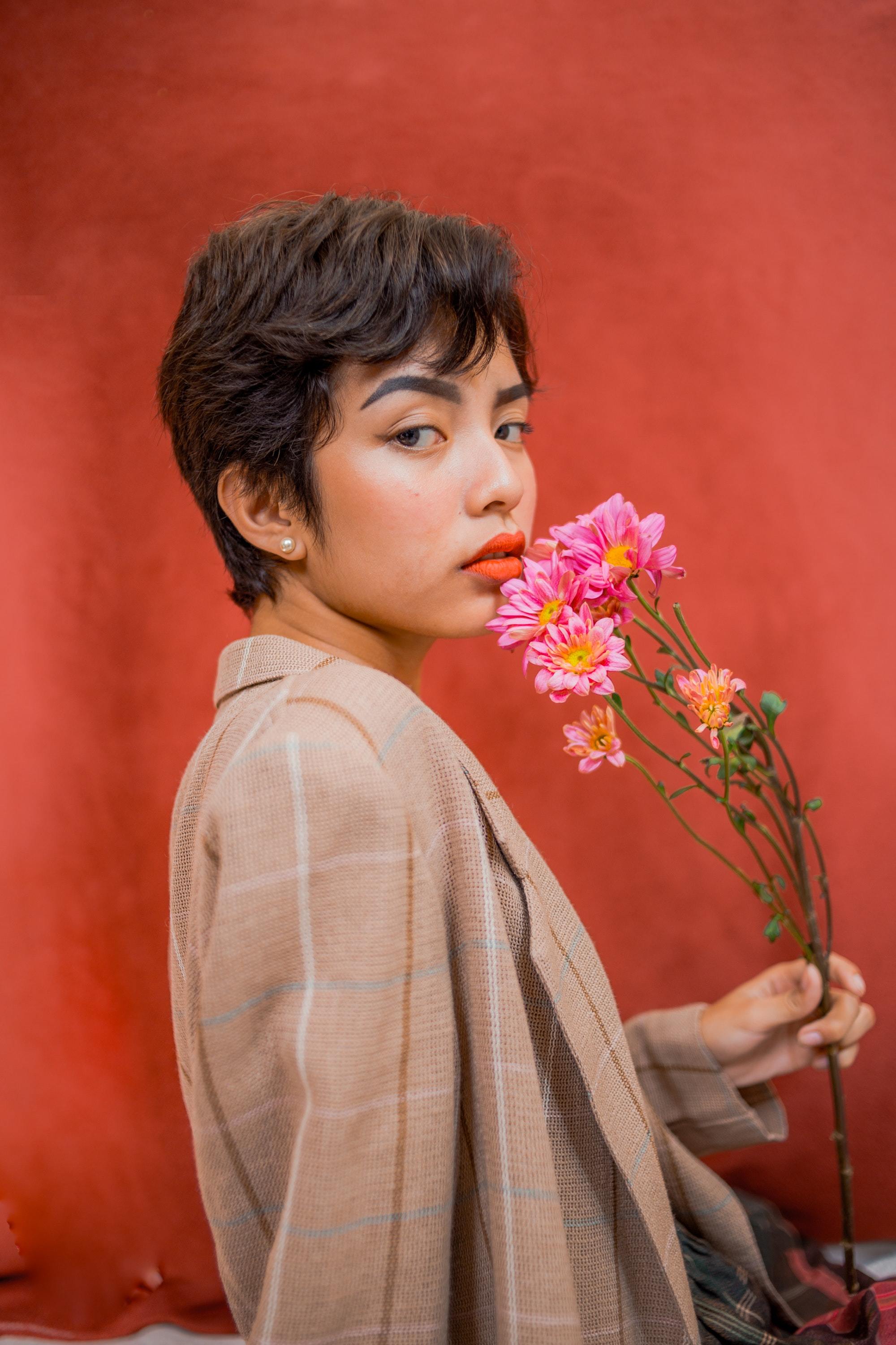 Asian woman with a wavy pixie cut wearing a brown blazer and holding flowers.