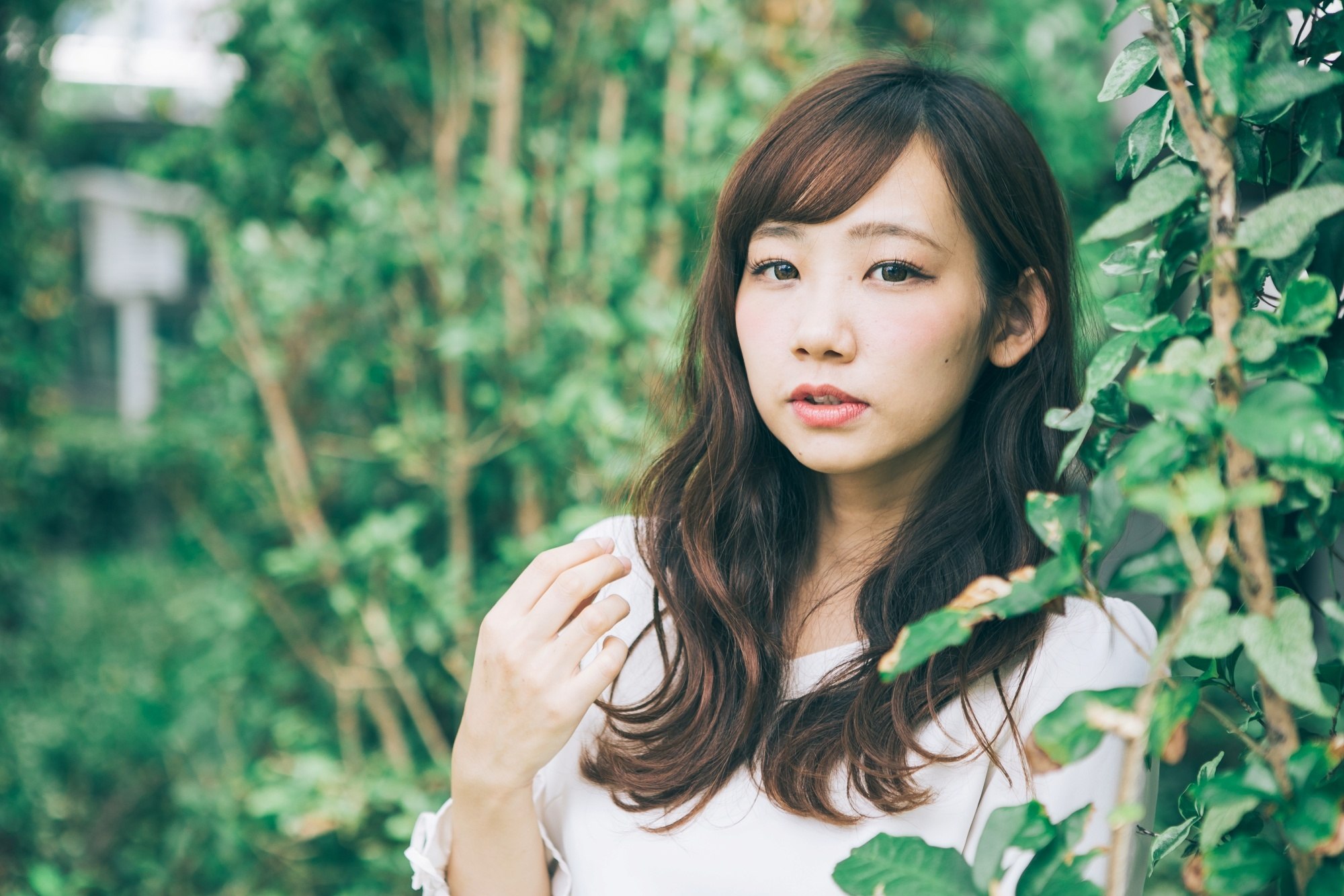 Asian woman with long hair and side-swept bangs standing among plants.