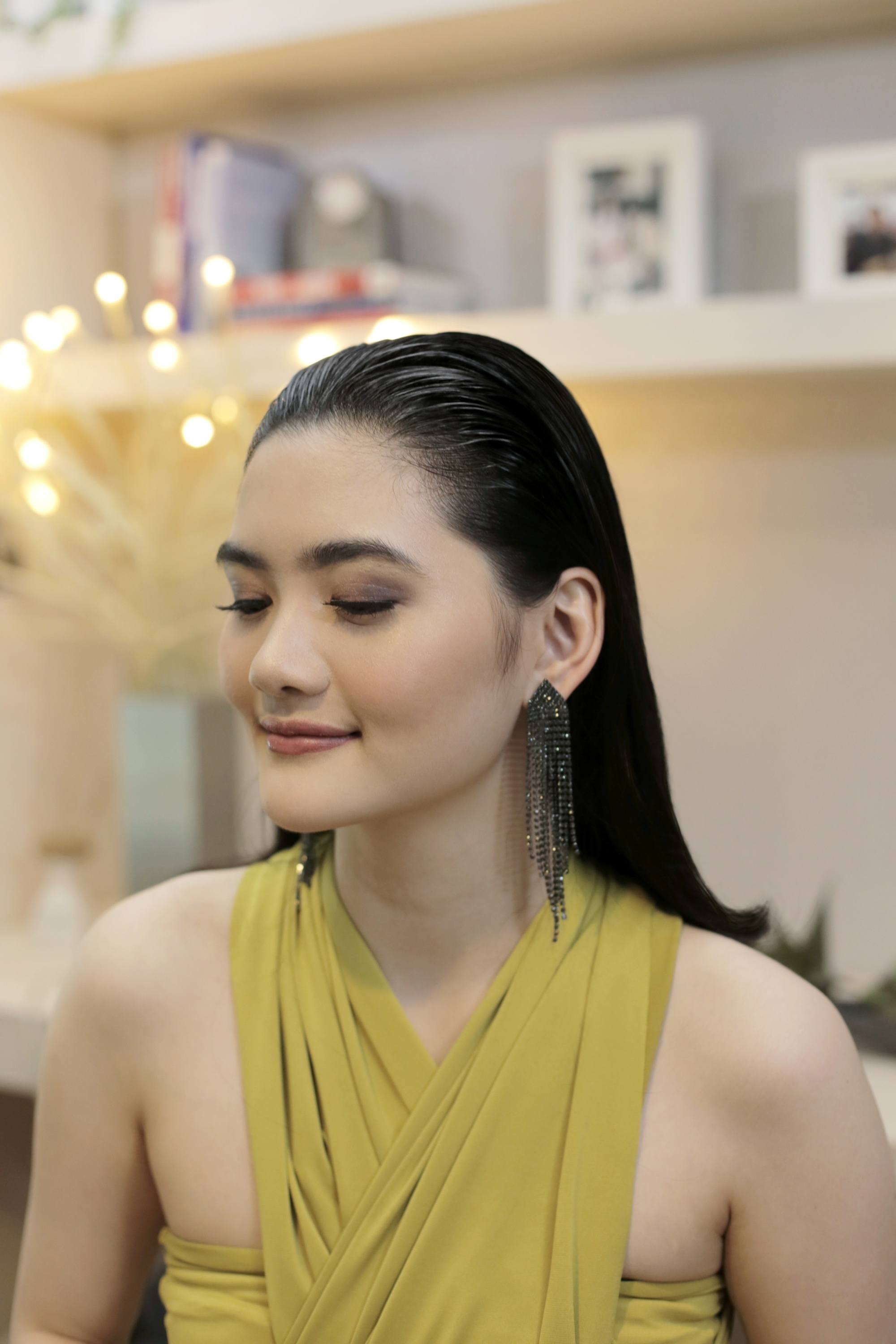 Asian woman with long hair in a slicked-back hairstyle wearing a mustard-colored dress.