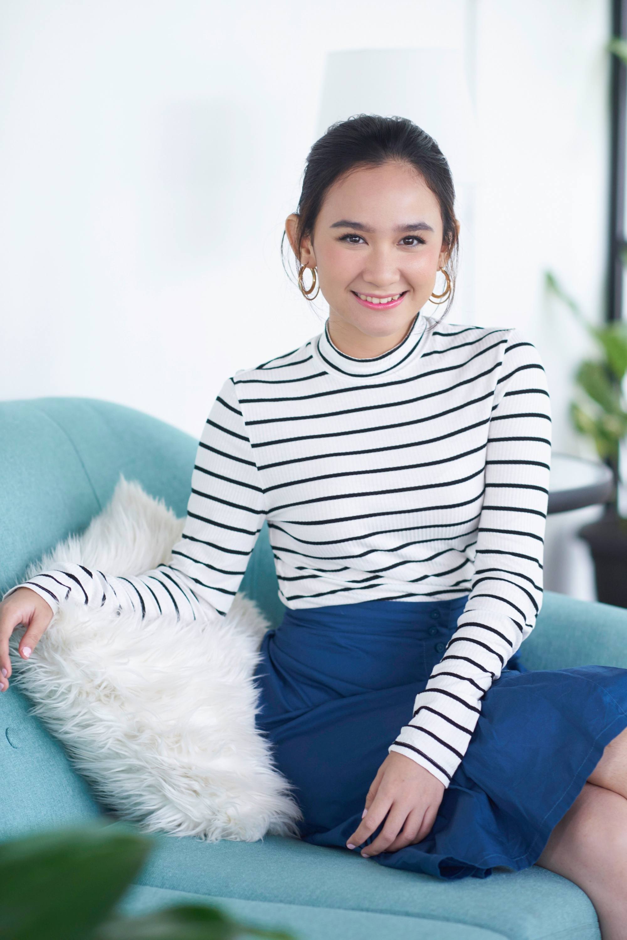 Asian woman with a bun hairstyle sitting on a blue chair.