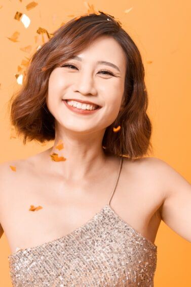 Asian woman with a short party hairstyle smiling while confetti is falling.