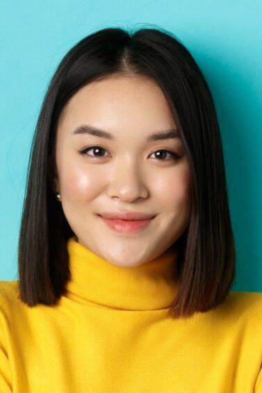 Asian woman with a lob haircut wearing a yellow turtleneck.